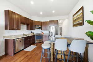 Kitchen featuring stainless steel appliances, recessed lighting, dark wood finish cabinets, dark wood finished floors, and a kitchen bar