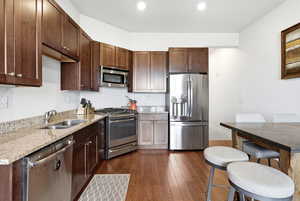 Kitchen featuring stainless steel appliances, light stone countertops, dark wood finish cabinets, and dark wood finished floors
