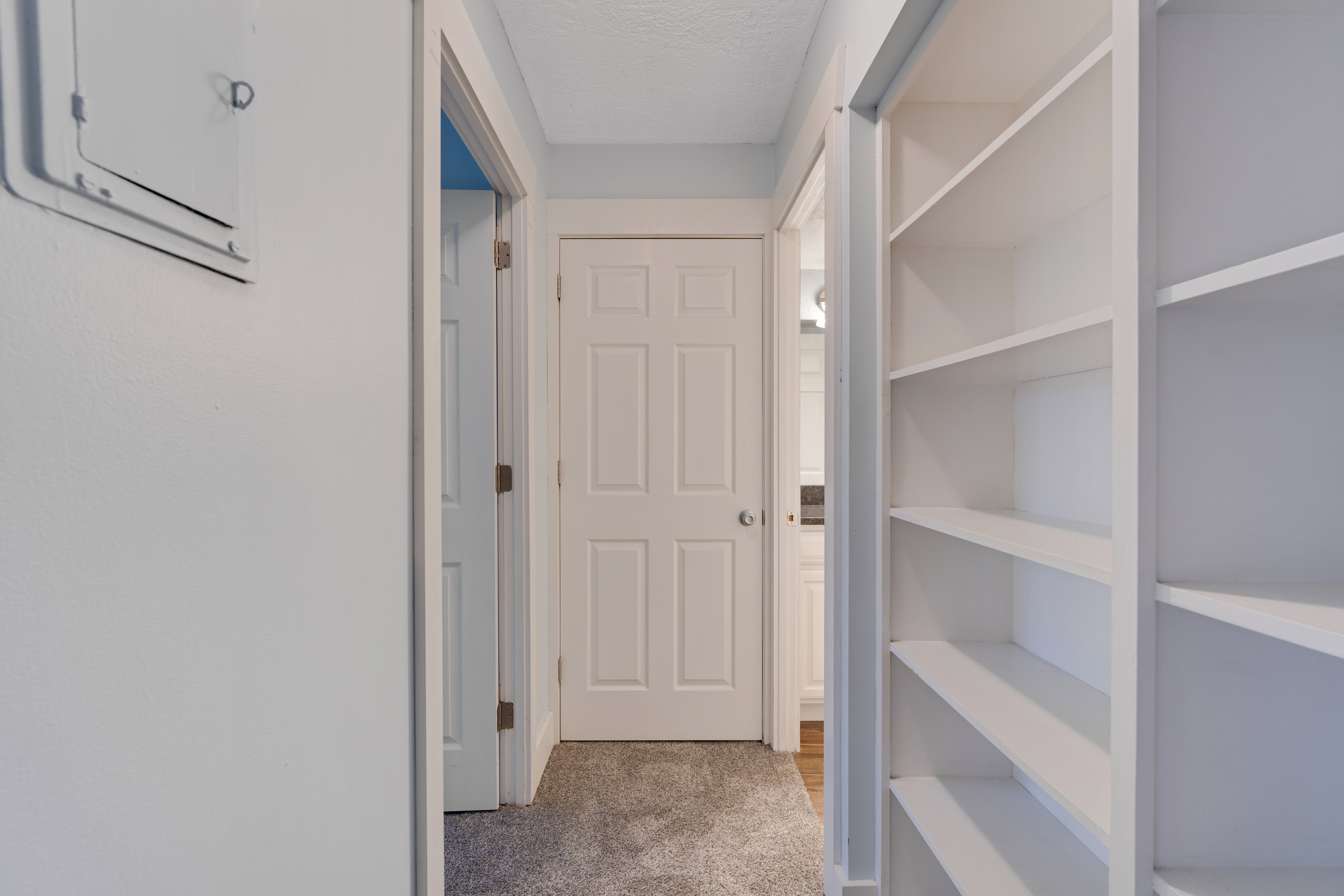 Corridor featuring light colored carpet and a textured ceiling