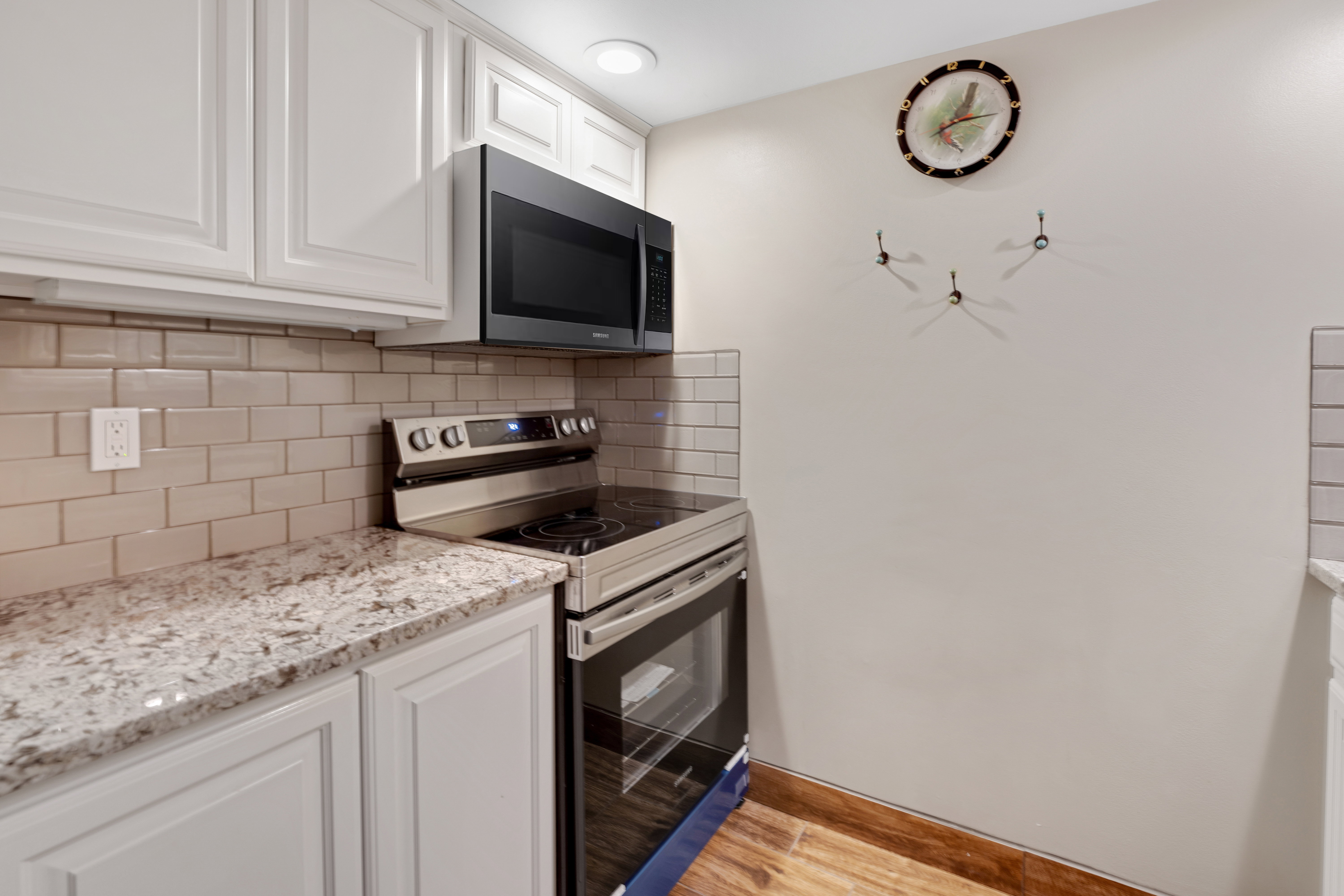 Kitchen with stainless steel appliances, white cabinetry, backsplash, light wood-style floors, and light stone countertops
