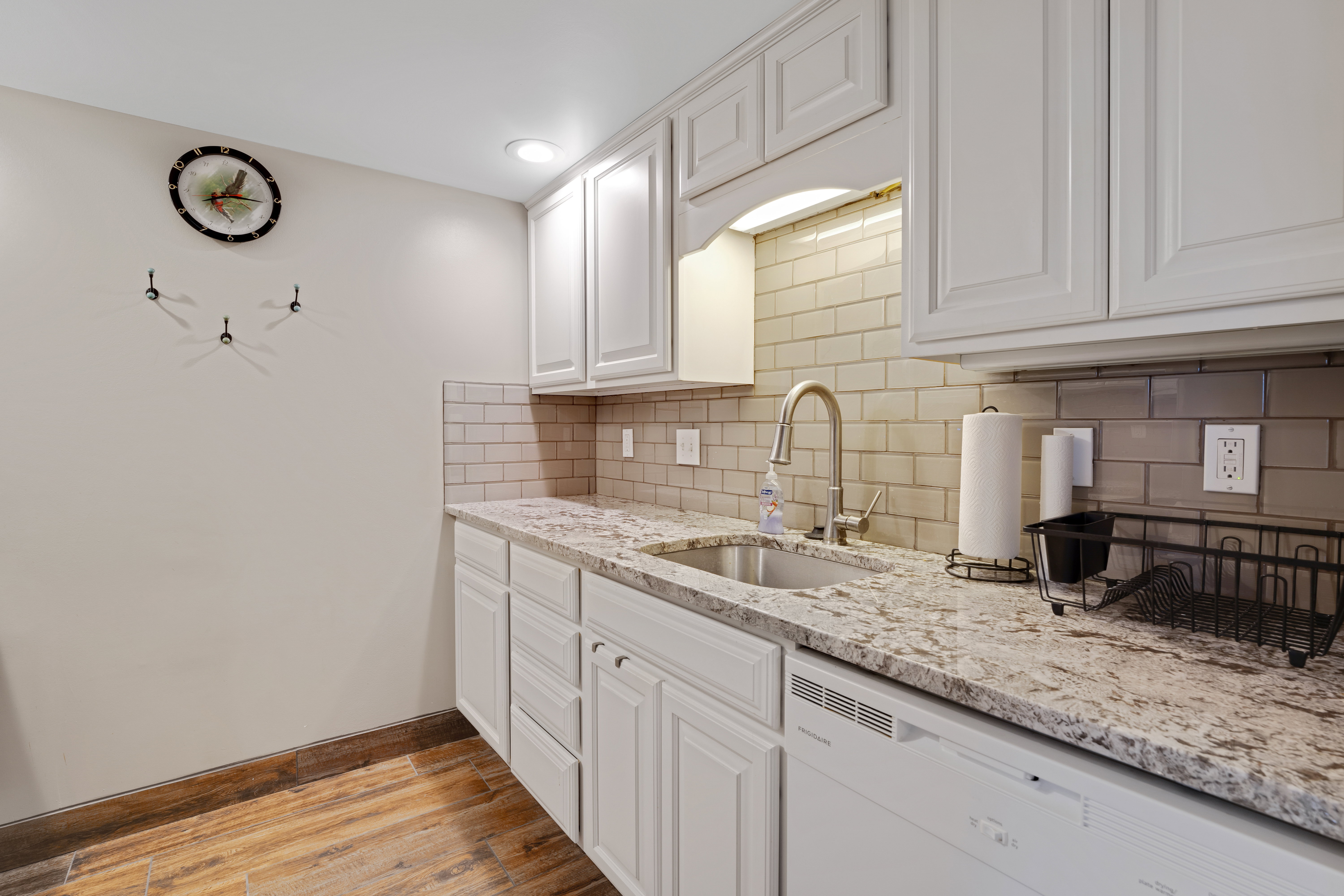 Kitchen with light stone countertops, white cabinetry, dishwasher, light wood-style flooring, and tasteful backsplash