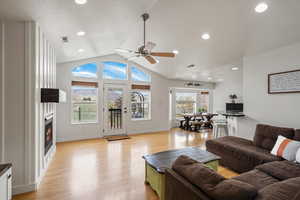 Living room featuring a ceiling fan, light wood-type flooring, a warm lit fireplace, and recessed lighting