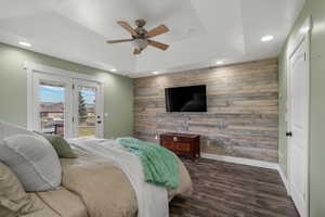 Bedroom featuring wood walls, an accent wall, access to outside, dark wood-style floors, and a ceiling fan