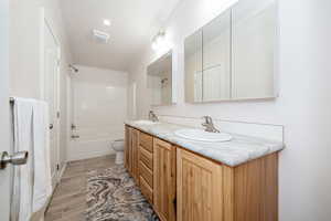 Full bath featuring double vanity, washtub / shower combination, and wood tiled floors