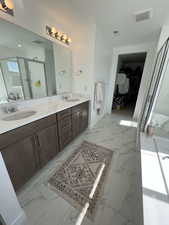 Full bathroom with double vanity, a spacious closet, light marble finish flooring, and a stall shower