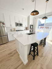 Kitchen with stainless steel appliances, white cabinets, light wood-type flooring, a center island with sink, and a kitchen breakfast bar
