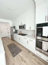 Kitchen with stainless steel appliances, white cabinetry, light wood-type flooring, and decorative backsplash