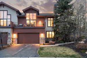 View of front facade with stone siding, a garage, driveway, a balcony, and stucco siding