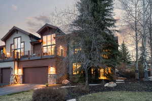 View of front of home with concrete driveway, stone siding, a balcony, a garage, and stucco siding