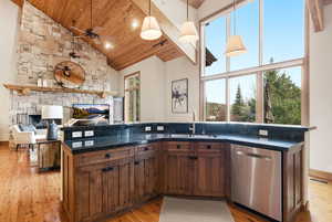 Kitchen featuring open floor plan, a stone fireplace, light wood-type flooring, dishwasher, and a vaulted wooden ceiling
