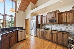 Kitchen with dark stone counters, stainless steel appliances, light wood-style flooring, tasteful backsplash, and decorative light fixtures