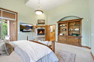 Bedroom with a stone fireplace, light carpet, a high ceiling, and access to exterior