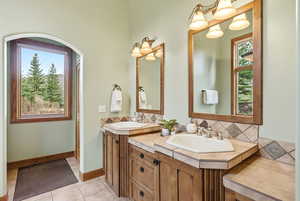 Bathroom with double vanity, light tile patterned flooring, and tasteful backsplash