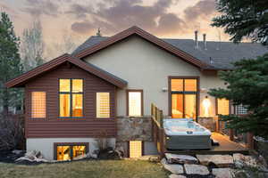View of front of property featuring a hot tub, a deck, stucco siding, stone siding, and roof with shingles