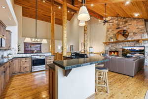 Kitchen featuring a kitchen bar, open floor plan, a fireplace, ceiling fan, and a high wooden beamed ceiling