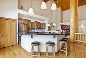Kitchen featuring a breakfast bar area, wood finish cabinetry, stainless steel appliances, light wood-type flooring, and vaulted ceiling