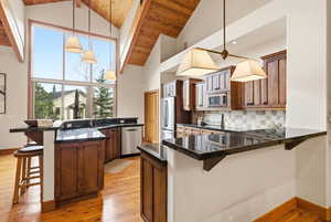 Kitchen with a kitchen bar, a peninsula, light wood-style flooring, decorative light fixtures, and a vaulted wooden ceiling