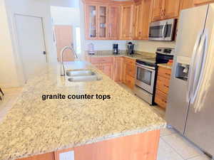Kitchen with light tile patterned flooring, glass insert cabinets, stainless steel appliances, and light granite countertops