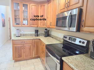 Kitchen featuring stainless steel appliances, light granite counters, glass insert cabinets, light tile patterned floors, and wood finish cabinetry
