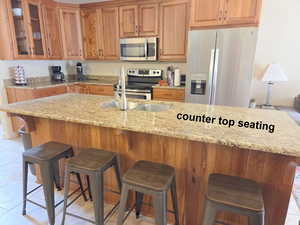 Kitchen featuring stainless steel appliances, light granite counters, glass insert cabinets, wood finish cabinetry, and a breakfast bar area