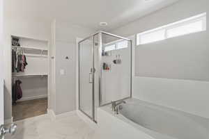 Bathroom with a walk in closet, a stall shower, a bath, and light marble finish floors