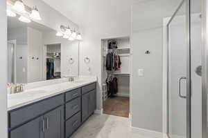 Bathroom featuring a shower stall, double vanity, light marble finish flooring, and a walk in closet