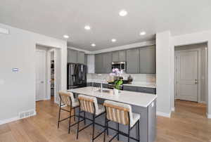Kitchen with gray cabinetry, a kitchen breakfast bar, an island with sink, light wood finished floors, and recessed lighting