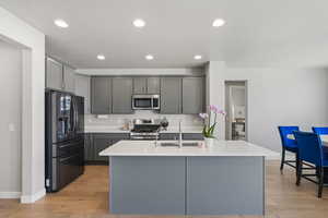Kitchen with gray cabinets, stainless steel appliances, light wood finished floors, an island with sink, and recessed lighting