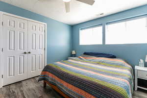 Bedroom with dark wood-type flooring, a closet, a ceiling fan, and a textured ceiling