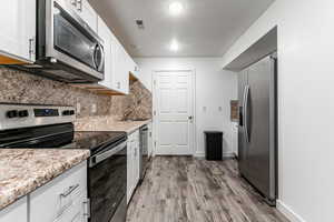 Kitchen with stainless steel appliances, white cabinetry, backsplash, light wood-type flooring, and light stone countertops