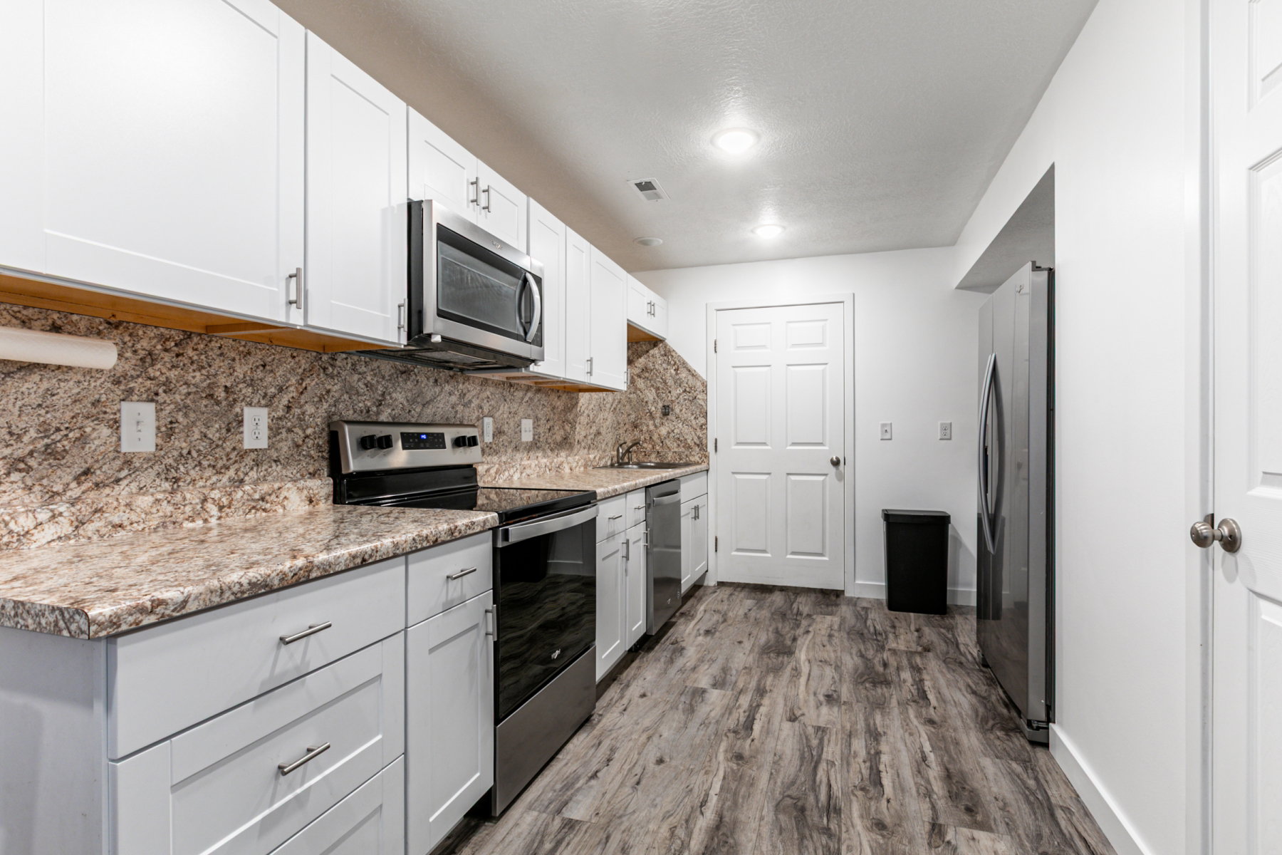 Kitchen featuring stainless steel appliances, white cabinetry, dark wood-style floors, tasteful backsplash, and light stone countertops
