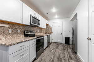 Kitchen featuring stainless steel appliances, white cabinetry, dark wood-style floors, tasteful backsplash, and light stone countertops
