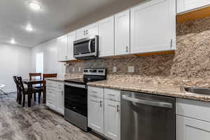 Kitchen featuring stainless steel appliances, white cabinetry, dark wood-type flooring, a textured ceiling, and tasteful backsplash