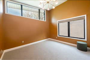 Carpeted spare room with suspended lighting and baseboards