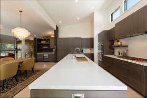Kitchen with dark wood finish cabinets, a spacious island, open shelves, light wood-style floors, and vaulted ceiling