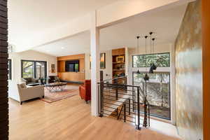 Hall featuring an upstairs landing, light wood-style floors, lofted ceiling, and recessed lighting