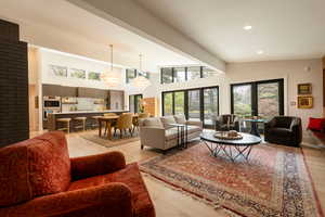 Living area with light wood-style flooring, hanging lights, and a high ceiling