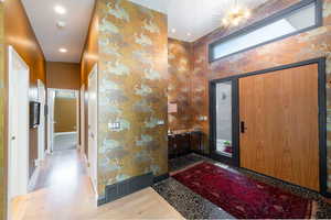 Foyer featuring light wood-style flooring, wallpapered walls, a high ceiling, recessed lighting, and arched walkways