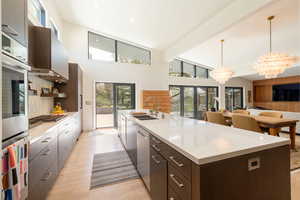 Kitchen with dark wood finish cabinets, a large island, suspended lighting, stainless steel appliances, and light wood-type flooring
