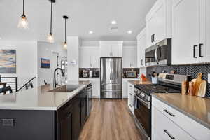 Two tone kitchen with stainless steel appliances, two tone cabinetry, light wood finished floors, decorative light fixtures, and a kitchen island with sink