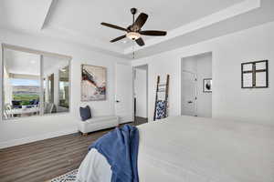 Bedroom featuring a raised ceiling, dark wood finished floors, a ceiling fan, and ensuite bath