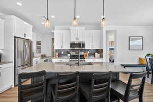 Kitchen featuring light wood-style flooring, stainless steel appliances, pendant lighting, an island with sink, and light stone countertops