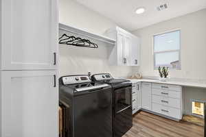 Laundry area featuring washing machine and dryer, light wood-type flooring, and cabinet space