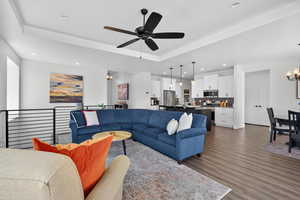 Living room featuring hanging lights, a ceiling fan, dark wood-style flooring, and a raised ceiling