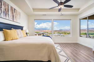 Bedroom with a raised ceiling, a mountain view, wood finished floors, and a ceiling fan
