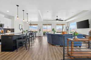 Living room with light wood finished floors, a ceiling fan, a raised ceiling, and hanging lights