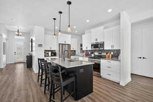 Two tone kitchen featuring stainless steel appliances, an island with sink, a kitchen breakfast bar, two tone cabinetry, and light wood-type flooring