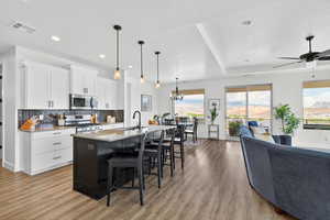 Two tone kitchen with a kitchen breakfast bar, an island with sink, open floor plan, two tone cabinets, and light wood finished floors