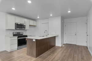 Kitchen with stainless steel appliances, a peninsula, recessed lighting, light wood-type flooring, and light stone countertops