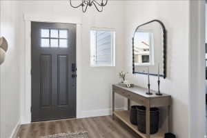 Entryway featuring a dark paneled door with glass inserts, wood-finish flooring, a decorative chandelier, a rectangular window with white trim, and white wall finishes